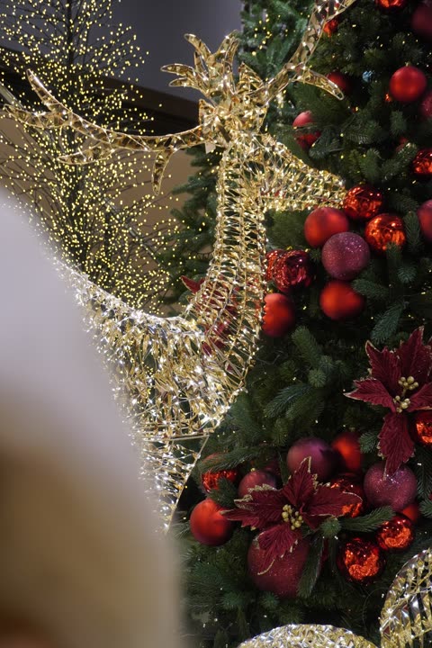 Renna luminosa accanto a un albero con fiori rossi